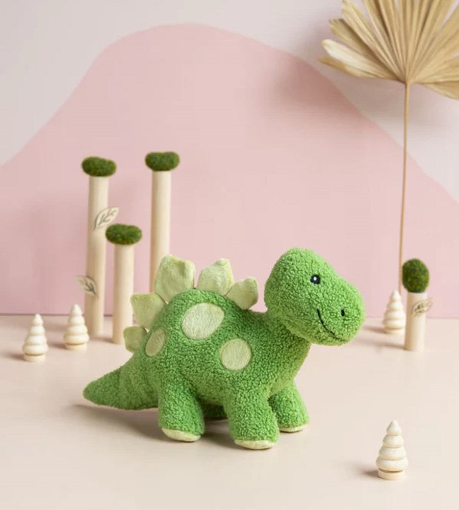 Green dinosaur plush toy on a light pink background with decorative elements.
