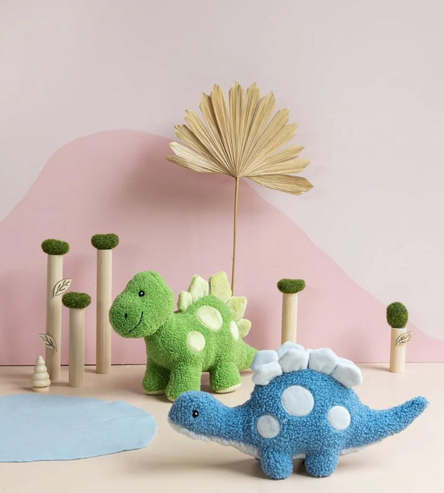 Two plush dinosaur toys, one green and one blue, on a beige surface with a pink background.