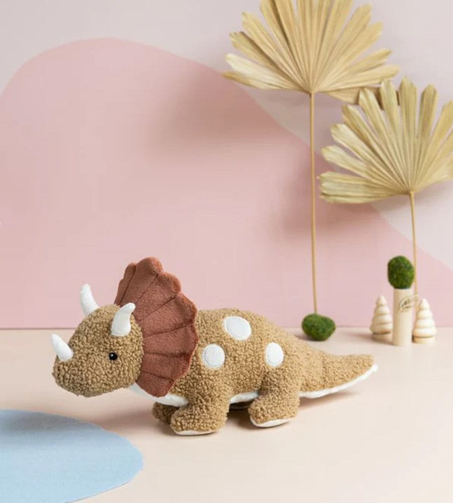Plush dinosaur toy with a brown back and white spots on a pink background with decorative plants.