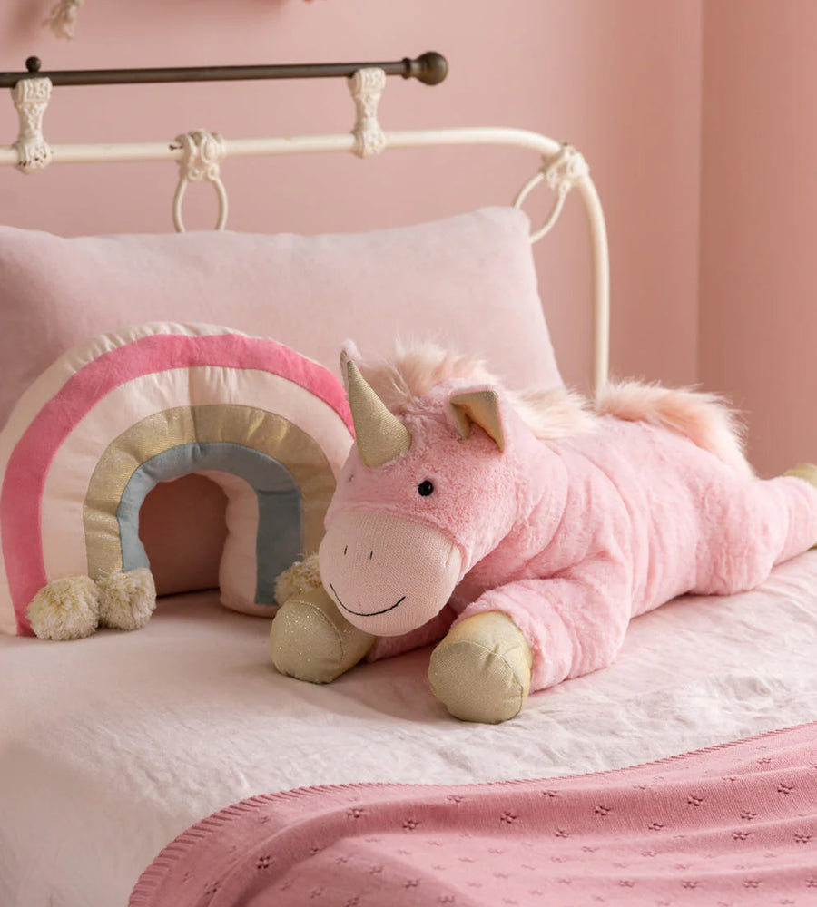 Pink unicorn plush toy and rainbow pillow on a bed with pink walls.