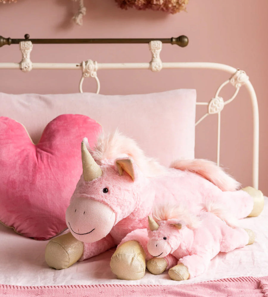 Pink plush unicorn toy on a bed with heart-shaped pillow and pink blanket