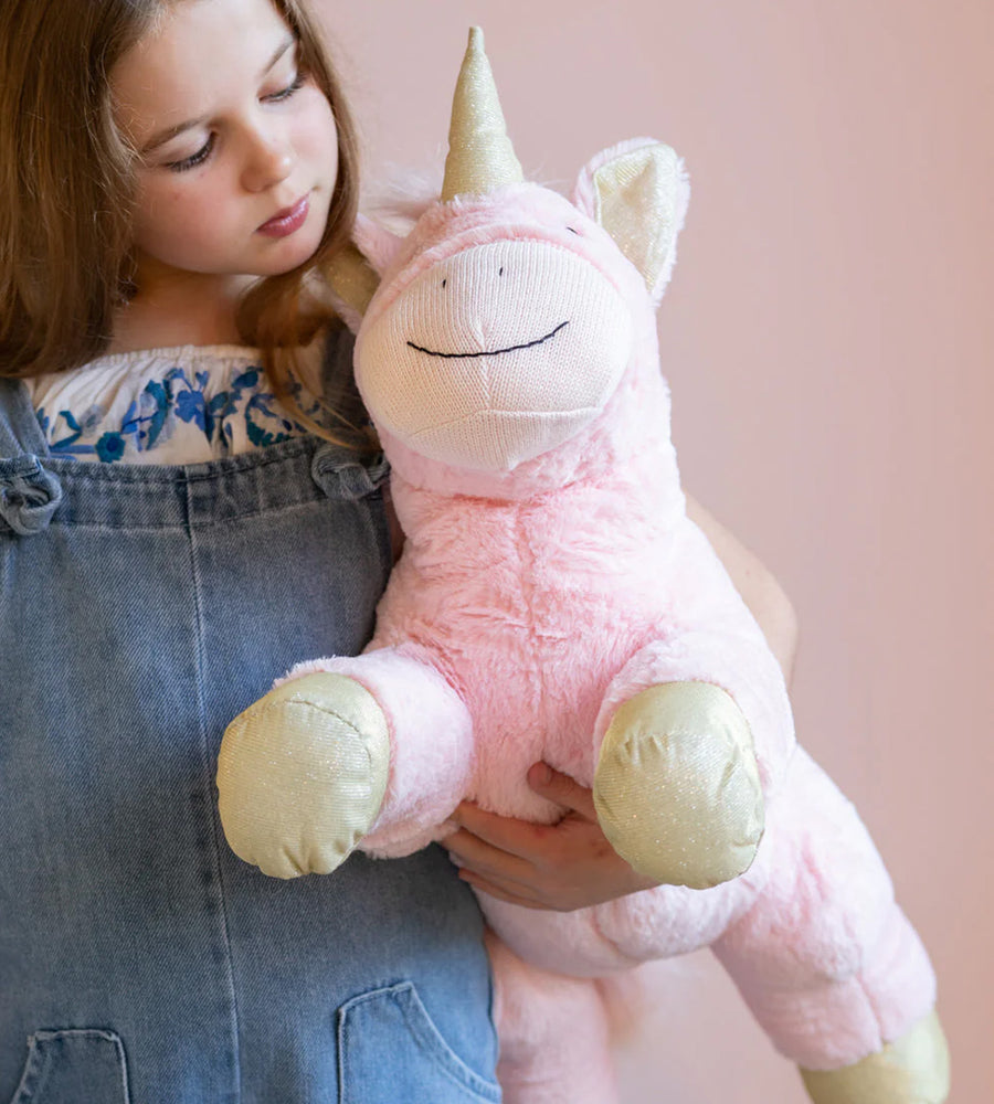 Child holding a pink unicorn plush toy against a soft pink background