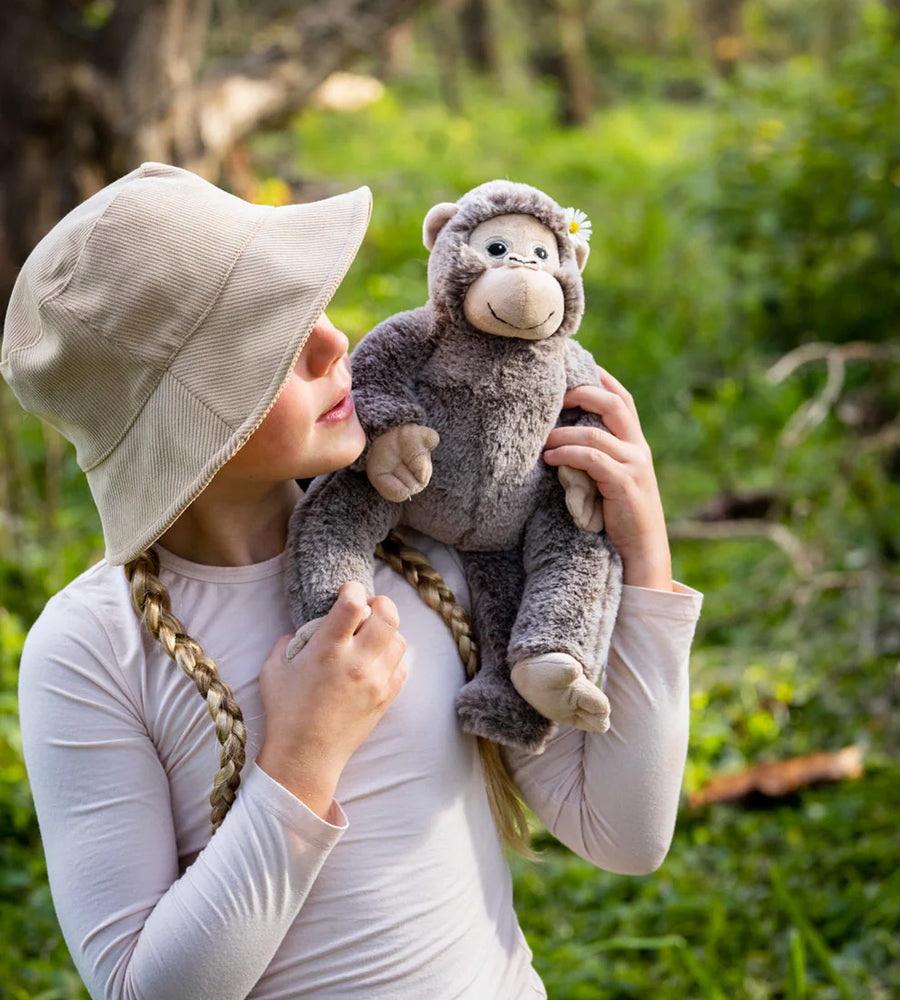 Child holding a plush monkey toy in a forest setting
