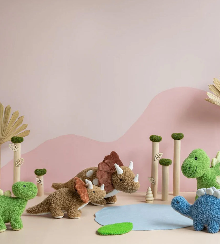 Plush dinosaur toys on a beige surface with a pink mountain background
