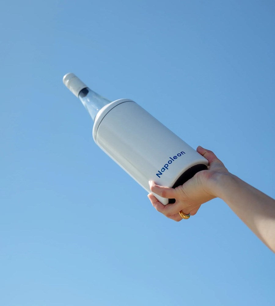 Hand holding a white Napoleon water bottle against a clear blue sky