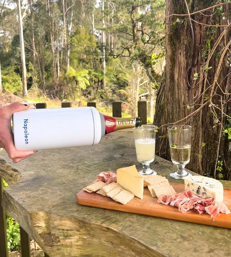 Person pouring wine into a glass on a wooden table with cheese and charcuterie, outdoors.