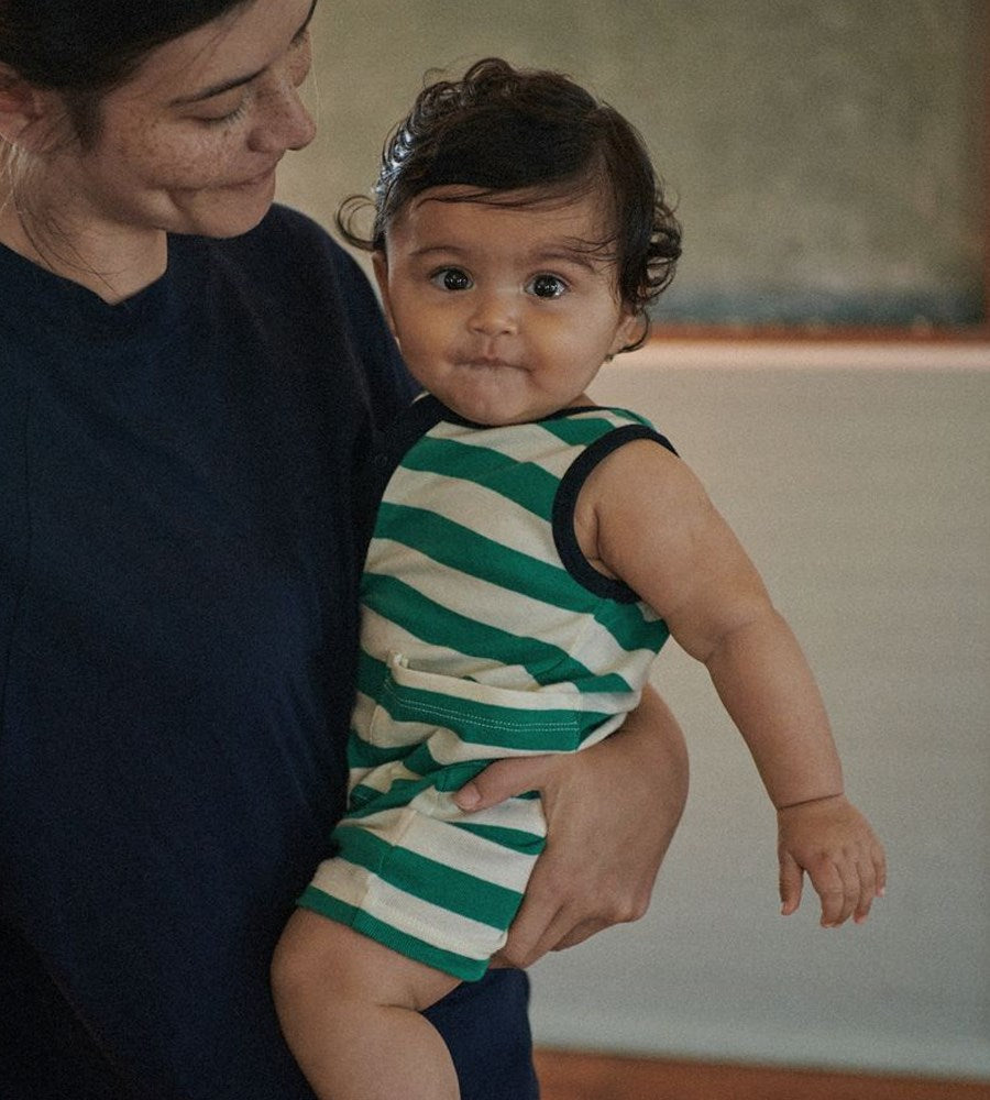 Woman holding a baby wearing a green and white striped onesie.