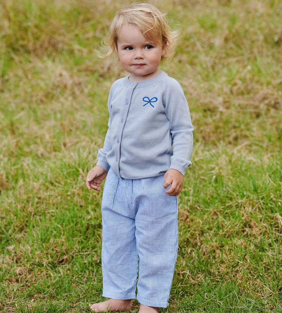 Child wearing a light blue outfit with a bow design in a grassy field