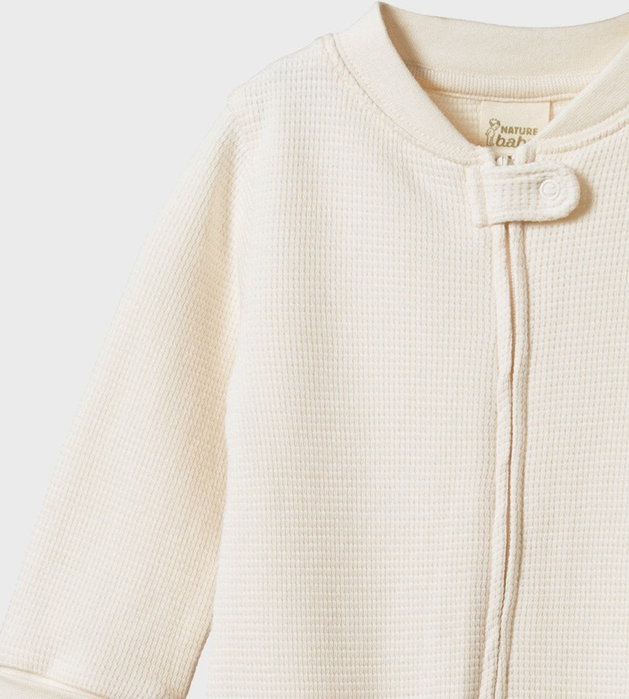 Close-up of a cream-colored baby onesie with a zipper on a light gray background.