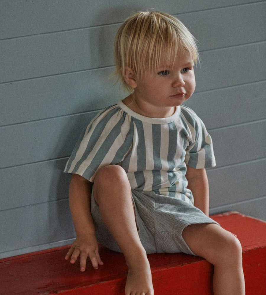 Child wearing a striped outfit sitting on a red surface against a gray wall