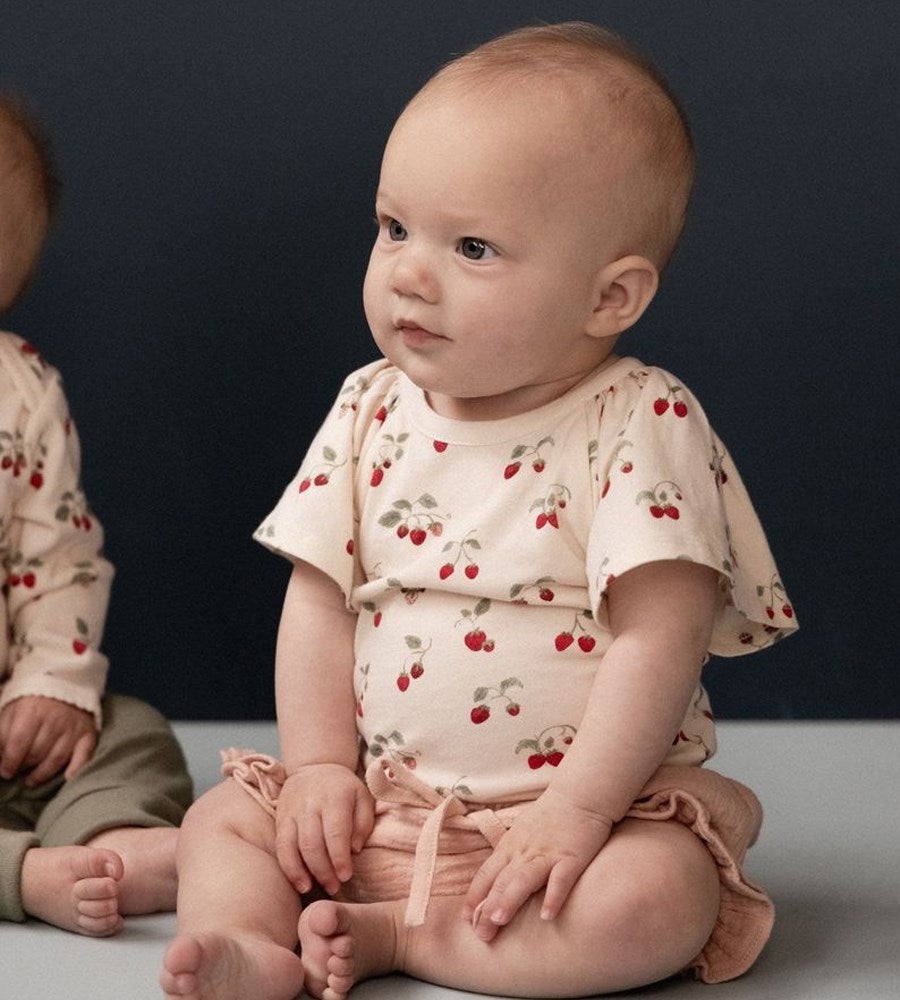 Baby wearing a cherry-patterned outfit sitting on a dark background
