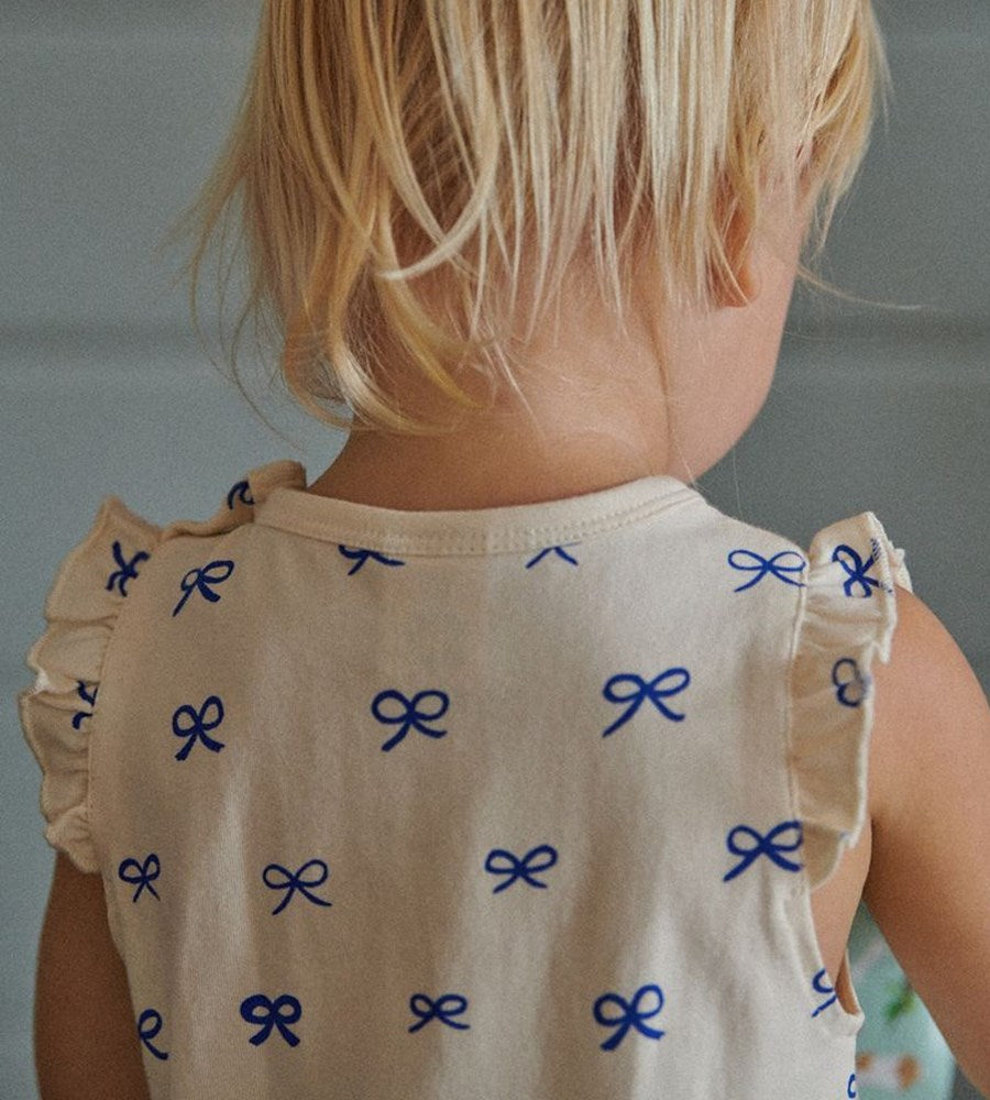 Child wearing a beige top with blue bow patterns against a neutral background