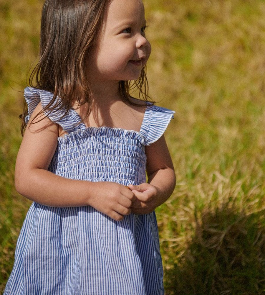 Young girl in a blue striped dress standing in a grassy field