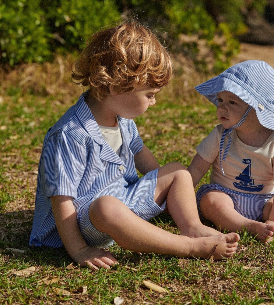 Two children sitting on the grass wearing matching blue and white outfits.