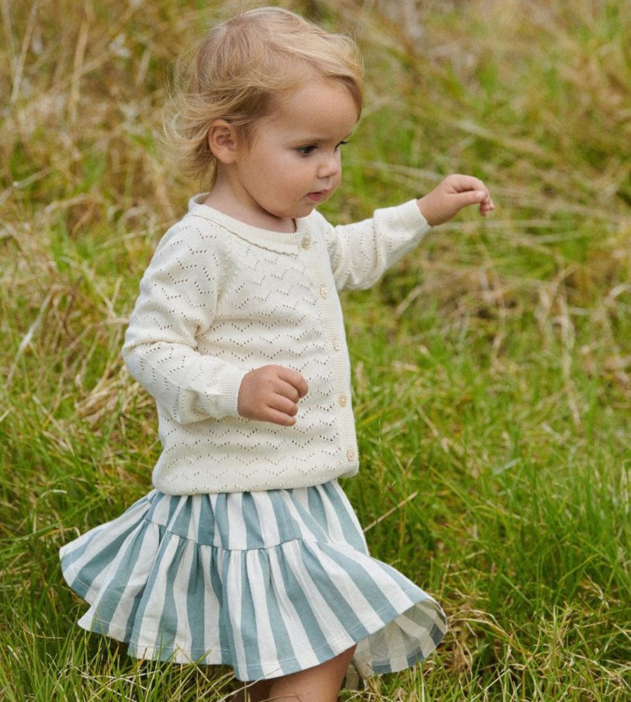 Young girl in a white sweater and striped skirt standing in a grassy field