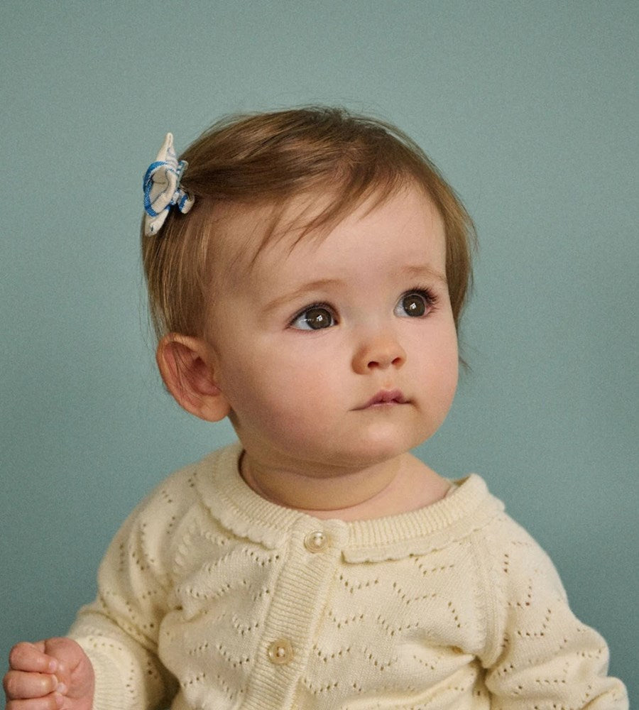 Baby wearing a cream-colored knitted sweater against a light blue background