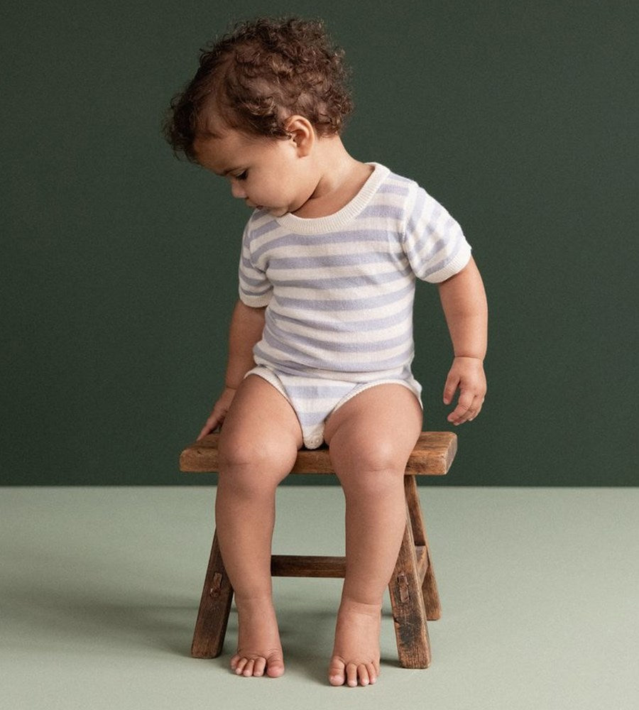 Child sitting on a wooden stool against a green background
