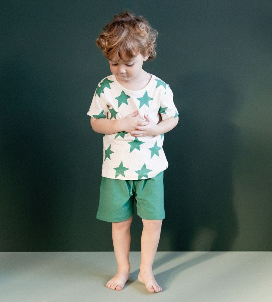 Child wearing a star-patterned shirt and green shorts against a dark background