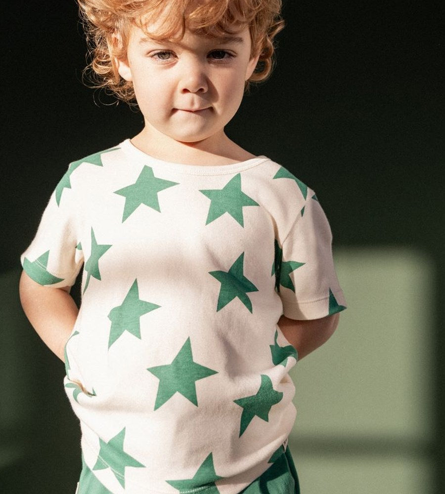 Child wearing a white shirt with green star patterns against a dark background