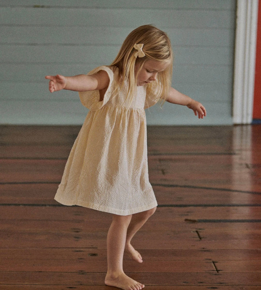 Young girl in a white dress standing on a wooden floor with a neutral background