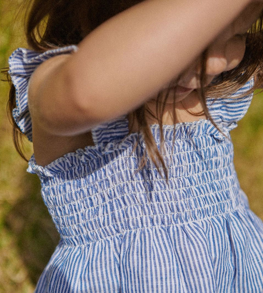 Close-up of a child wearing a blue and white striped dress with a blurred natural background