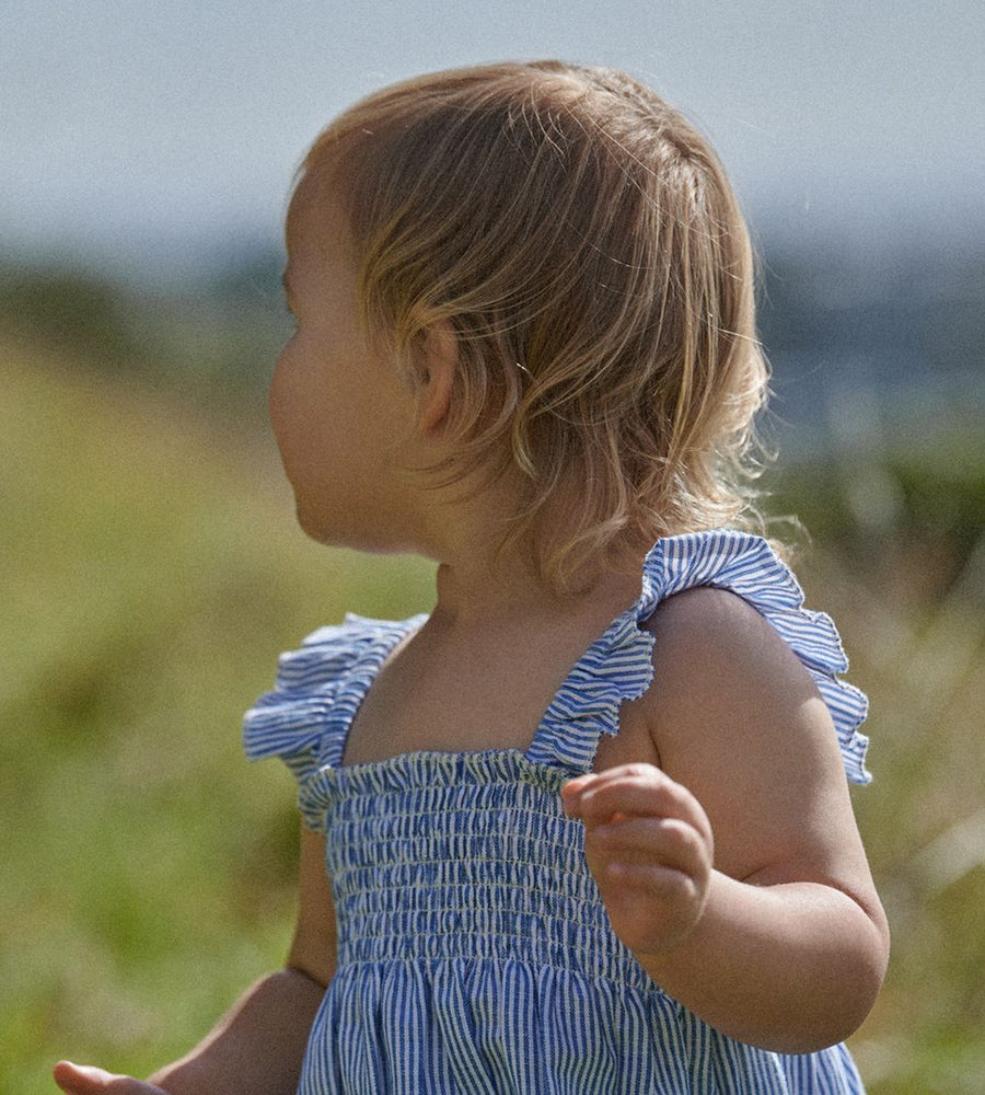Child wearing a blue dress with ruffled shoulders in an outdoor setting