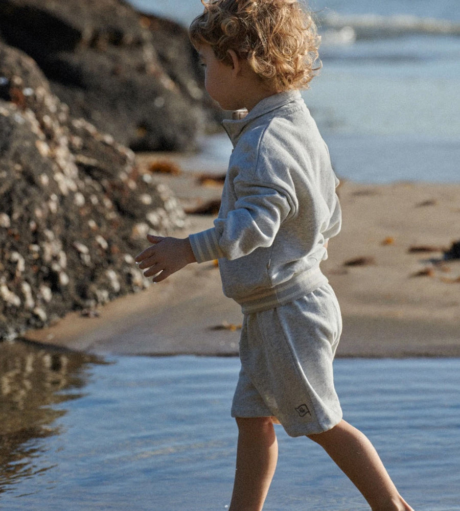 Child in a light gray outfit standing on a beach near water