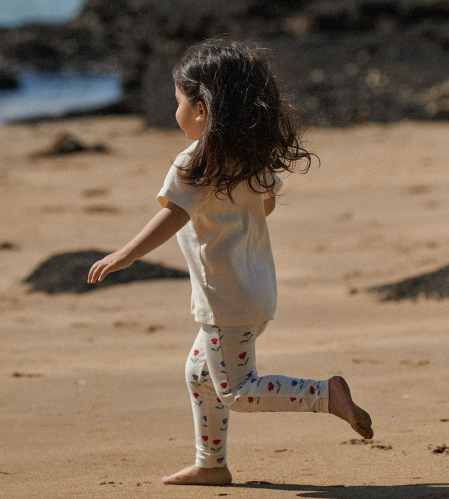 Child running on a sandy beach wearing a white shirt and patterned leggings.