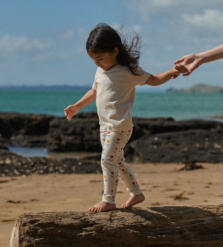 Child walking on a rock at the beach with an adult's hand holding theirs
