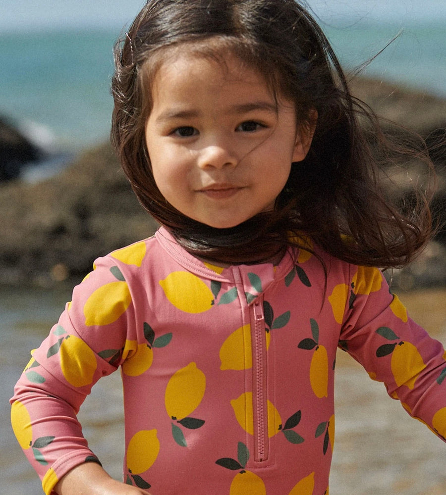 Child wearing a pink swimsuit with lemon pattern on a beach