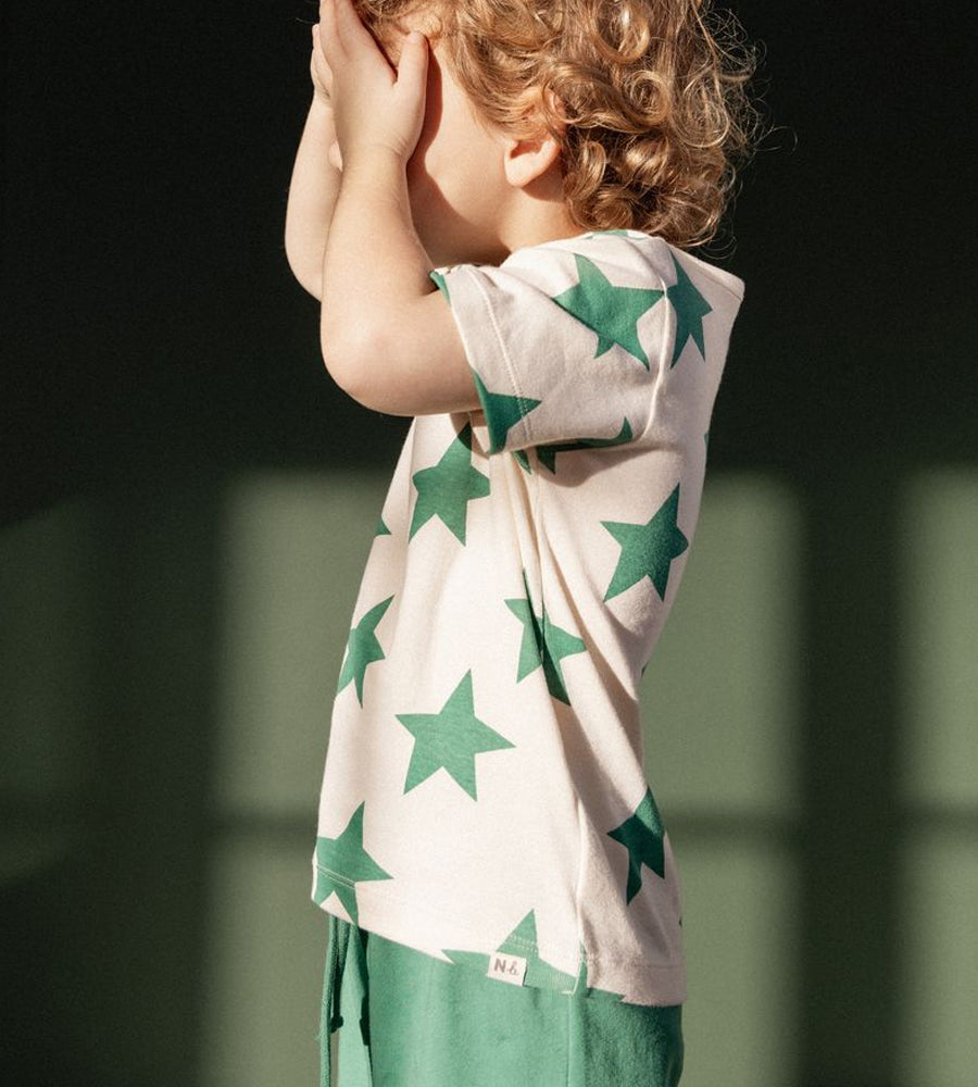Child wearing a white shirt with green star patterns and green pants against a dark background