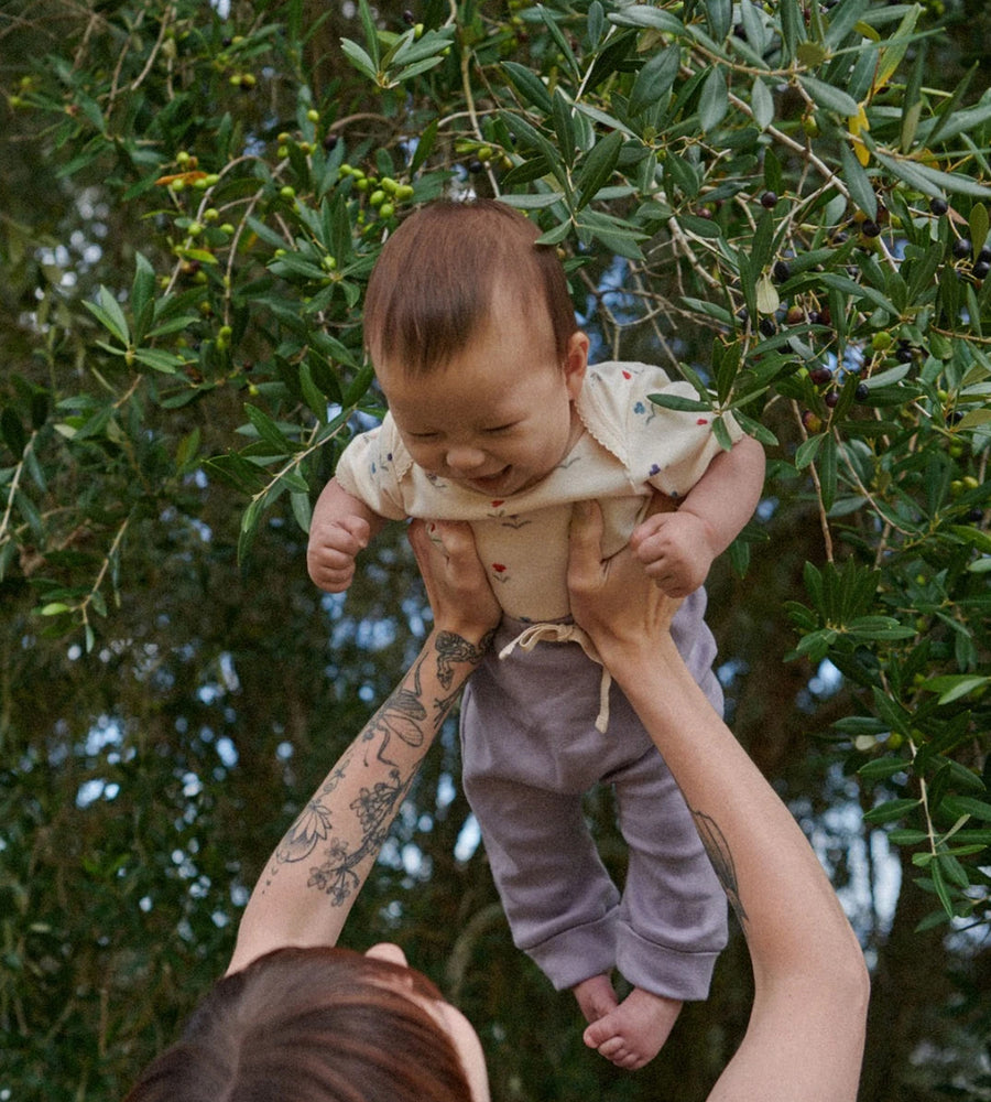 Person holding a baby in front of green foliage