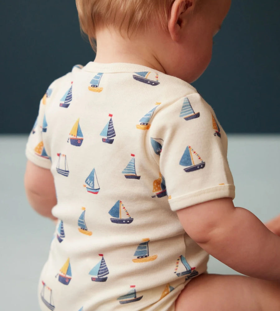 Baby wearing a onesie with sailboat pattern against a blue background