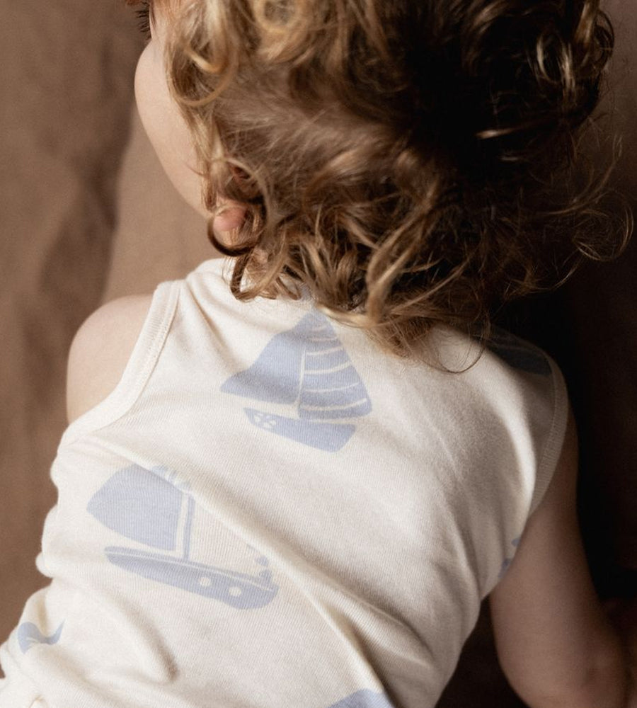 Child wearing a sleeveless shirt with sailboat patterns against a neutral background