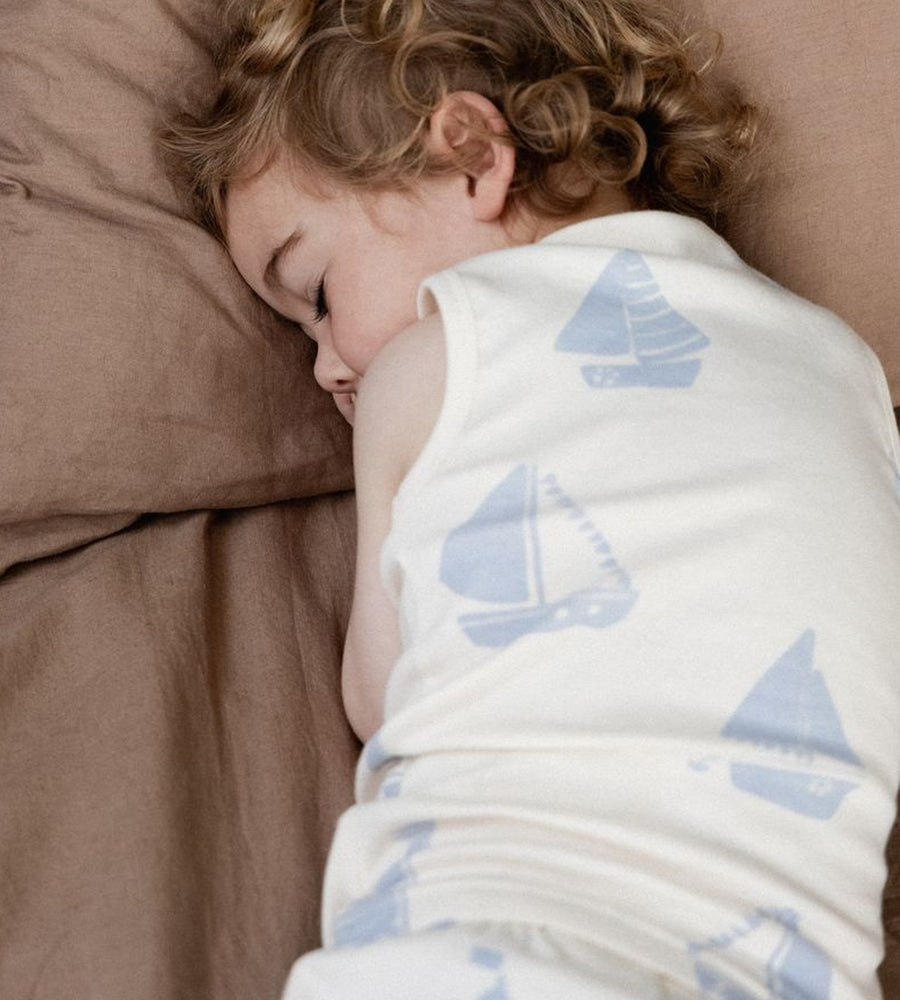 Child sleeping under a blanket with sailboat patterns on a brown pillow