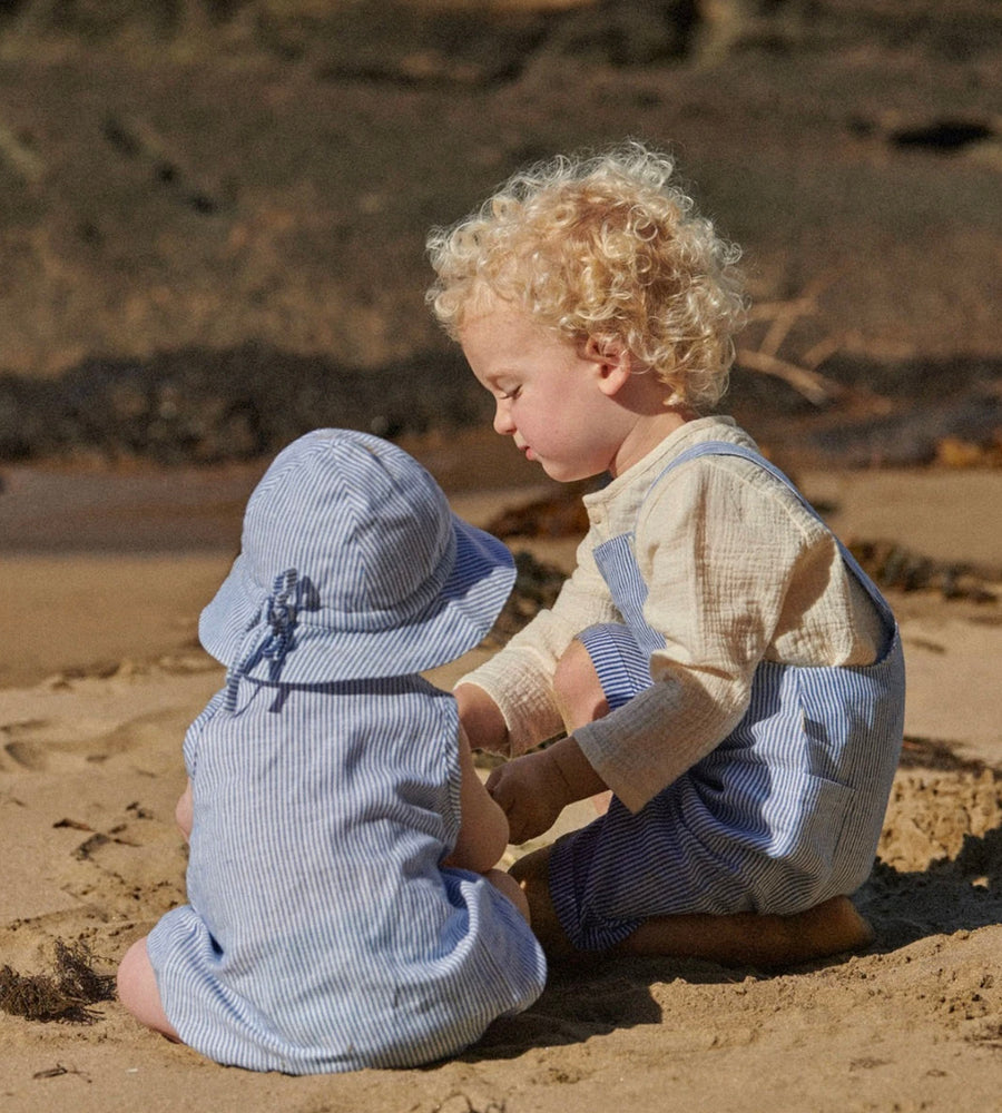 Two children in matching outfits sitting on a sandy beach.