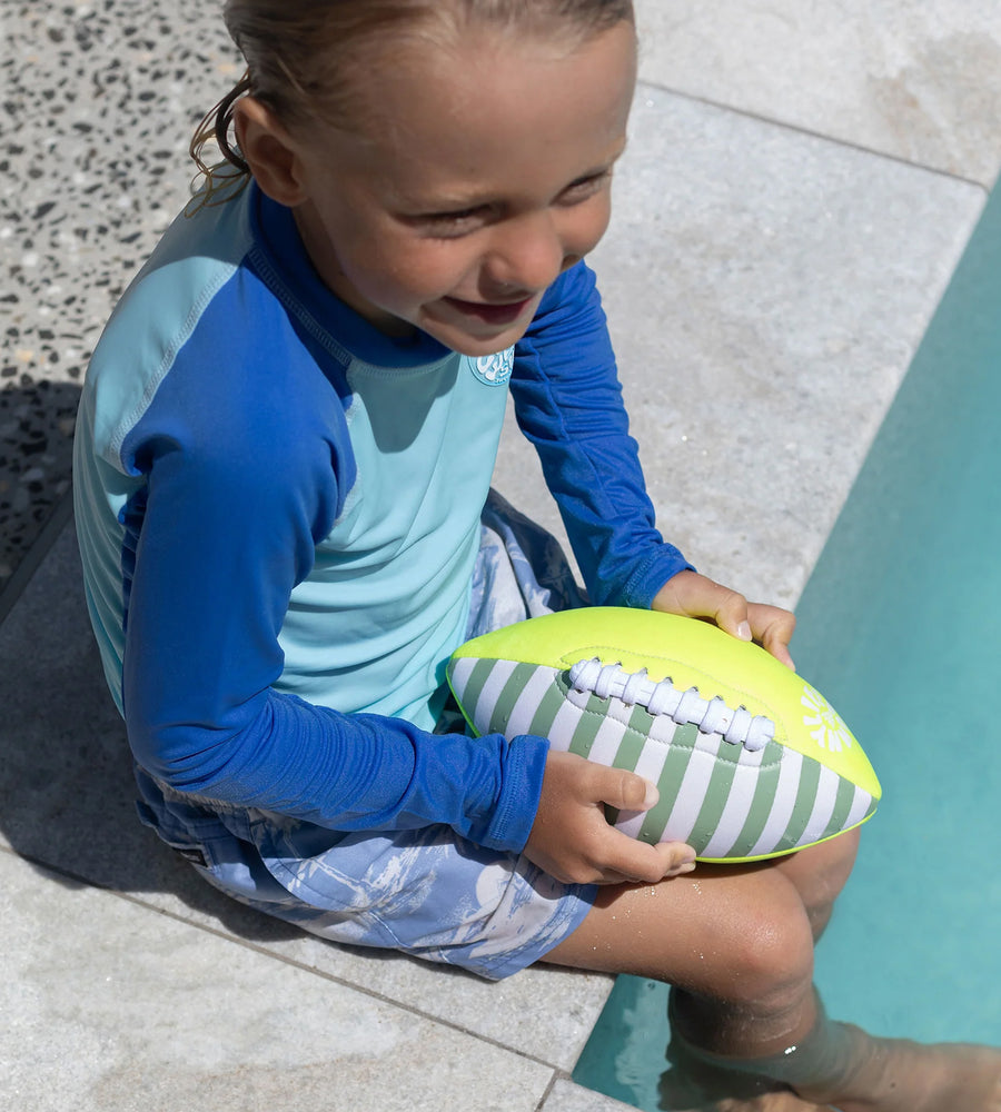Child holding a striped ball by a pool