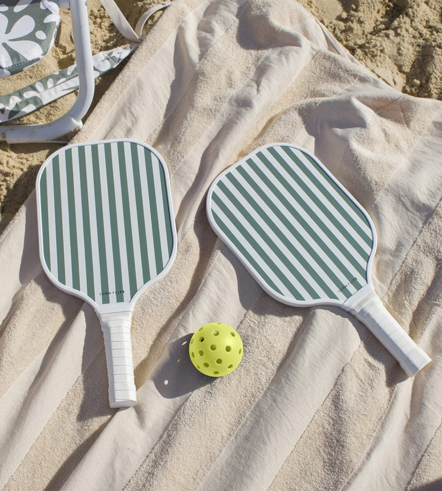 Two green and white striped pickleball paddles on a sandy surface with a yellow ball.