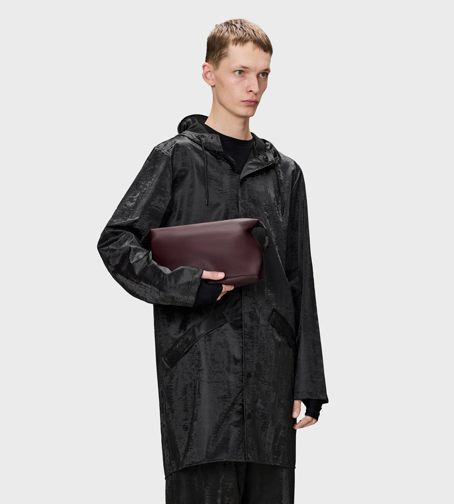 Person wearing a black raincoat holding a brown leather bag on a white background