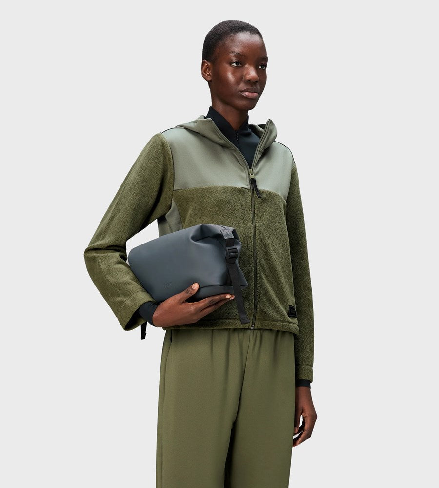 Person wearing a green and gray jacket holding a gray bag on a white background