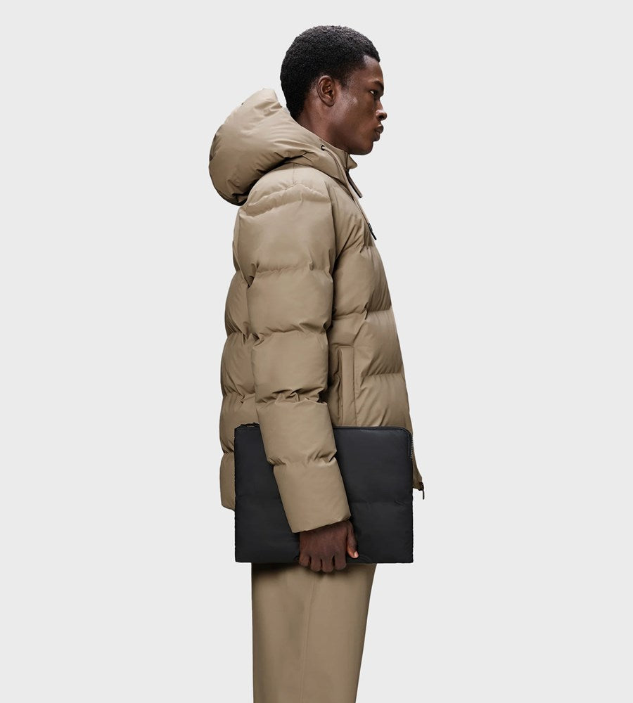 Person wearing a beige puffer jacket with black handbags on a white background