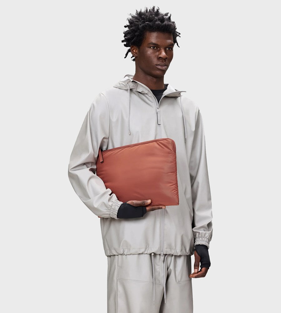 Person wearing a light gray tracksuit holding a brown pouch against a white background