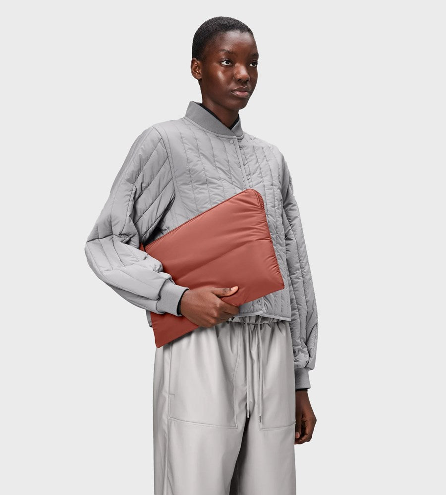 Person wearing a gray quilted sweater holding a pink clutch against a white background