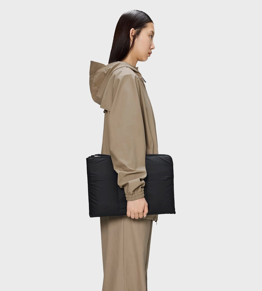 Person wearing a beige raincoat holding a black roll-up bag on a white background