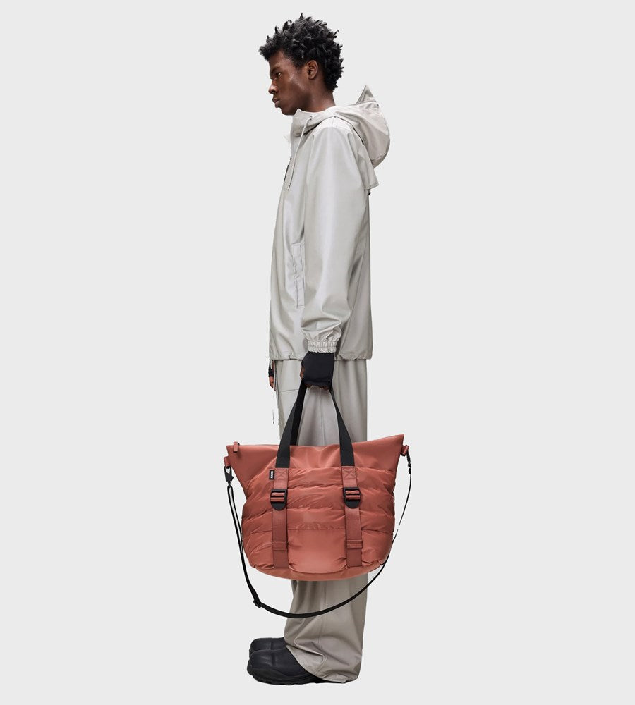Person holding a large pinkish-brown bag against a plain background