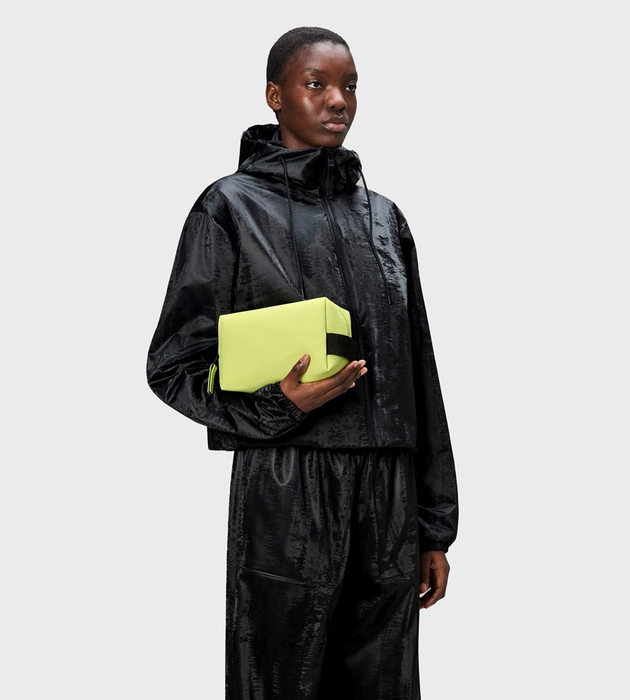 Person wearing a black outfit holding a yellow cube against a light gray background