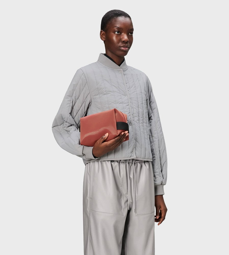 Person wearing a gray outfit holding a pink box against a white background