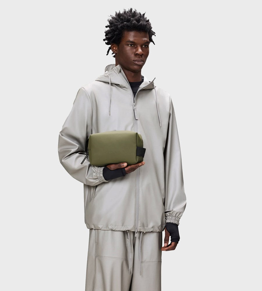 Person wearing a light gray outfit holding a green rectangular object against a white background