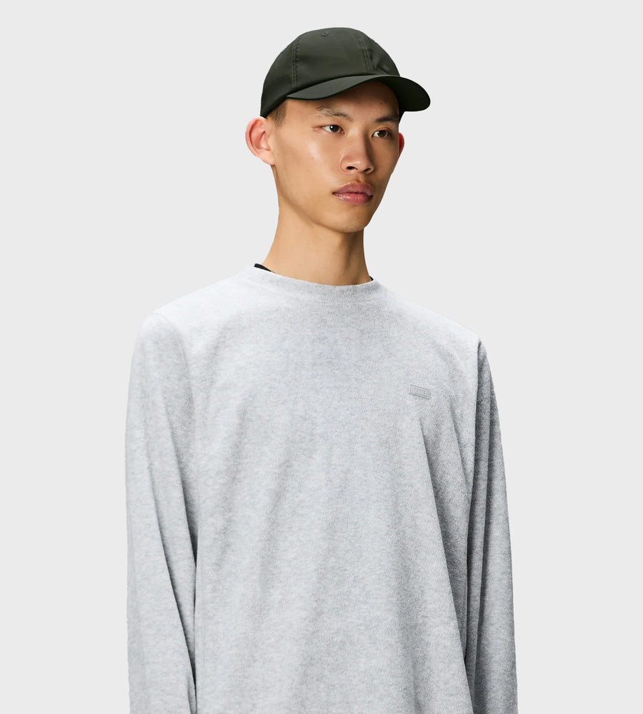 Person wearing a gray sweatshirt and green cap on a light gray background