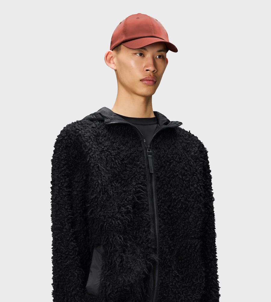 Person wearing a black sherpa jacket and red cap on a light gray background
